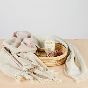 Handwoven in Peru: Beautiful baby alpaca blanket in the colour combination grey, beige, natural and antique pink with eyelash fringes and high relief stripes. Ambience photo with Brooklyn Candle Studio candle "Santorini" and tray "Umi".